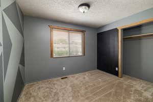 Unfurnished bedroom with a textured ceiling, carpet flooring, and a closet