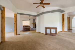 Unfurnished living room featuring carpet, vaulted ceiling, arched walkways, a fireplace, and ceiling fan