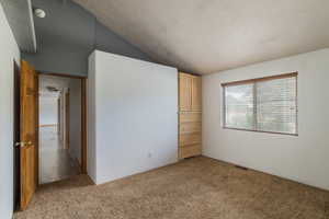Unfurnished bedroom with a textured ceiling, light carpet, and vaulted ceiling