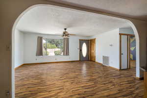Unfurnished living room featuring arched walkways, a textured ceiling, dark wood-style floors, and ceiling fan