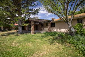 Rear view of house featuring stucco siding, a yard, a pergola, and a patio area