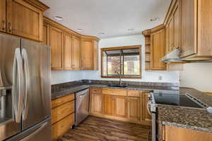 Kitchen with stainless steel appliances, dark wood finished floors, brown cabinets, recessed lighting, and open shelves