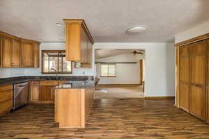 Kitchen featuring brown cabinets, dark stone counters, open floor plan, dishwasher, and a textured ceiling