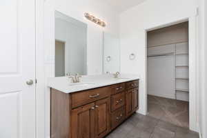 Bathroom featuring double vanity, dark tile patterned flooring, and a spacious closet