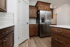 Kitchen featuring stainless steel fridge with ice dispenser, decorative backsplash, light wood-type flooring, light stone countertops, and recessed lighting