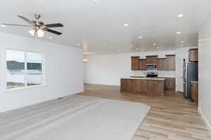 Kitchen with open floor plan, light countertops, a kitchen island, appliances with stainless steel finishes, and light wood-style flooring