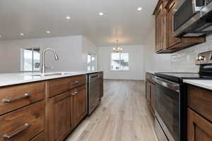 Kitchen with stainless steel appliances, light wood-type flooring, recessed lighting, hanging light fixtures, and tasteful backsplash
