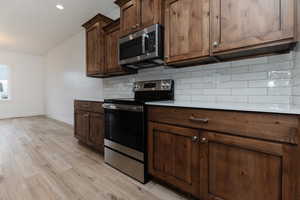Kitchen featuring appliances with stainless steel finishes, backsplash, light wood-style flooring, dark brown cabinets, and recessed lighting