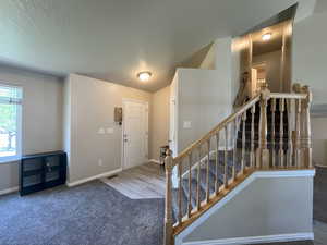 Entrance foyer with carpet floors, stairway, and a textured ceiling