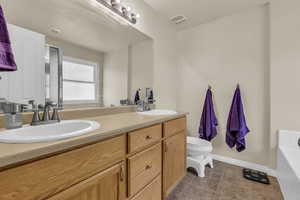 Full bath with double vanity, light tile patterned floors, and a bath