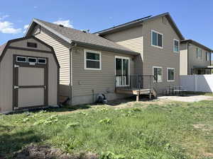 Back of house with a patio, roof with shingles, a shed, and a wooden deck