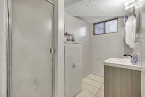 Bathroom featuring a textured ceiling, light tile patterned flooring, vanity, and a shower stall