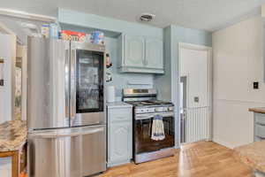Kitchen with appliances with stainless steel finishes, light wood-style flooring, a textured ceiling, wainscoting, and under cabinet range hood