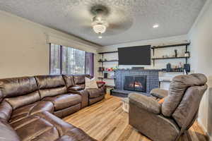 Living room with ornamental molding, a textured ceiling, wood finished floors, a fireplace, and recessed lighting