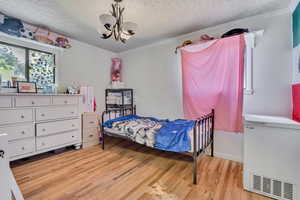 Bedroom with a textured ceiling, light wood-style flooring, crown molding, and a chandelier