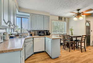Kitchen with a textured ceiling, light countertops, white dishwasher, light wood-style flooring, and ceiling fan