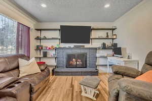 Living room featuring a textured ceiling, crown molding, wood finished floors, a brick fireplace, and recessed lighting