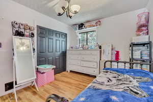 Bedroom featuring light wood-type flooring, a textured ceiling, a closet, crown molding, and a chandelier