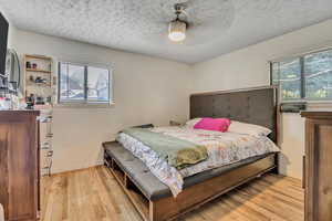 Bedroom featuring light wood-type flooring, multiple windows, a textured ceiling, and ceiling fan