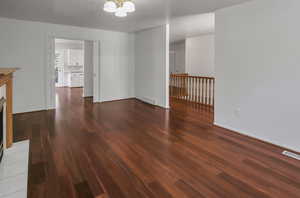 Unfurnished living room featuring dark wood-style flooring and a chandelier