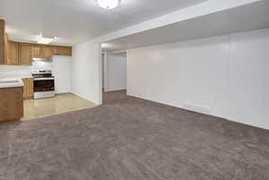 Kitchen featuring light countertops, stainless steel range with electric cooktop, brown cabinetry, open floor plan, and a textured ceiling