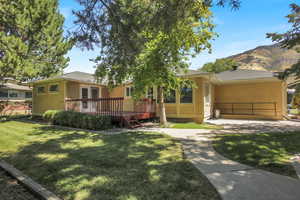 Single story home with a wooden deck, a front lawn, roof with shingles, and stucco siding