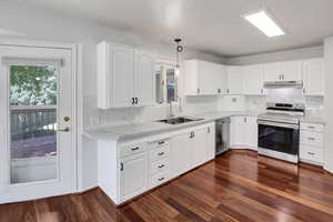 Kitchen featuring stainless steel appliances, pendant lighting, backsplash, white cabinetry, and dark wood-style floors