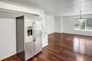 Kitchen featuring stainless steel refrigerator with ice dispenser, white cabinetry, dark wood finished floors, decorative light fixtures, and a chandelier