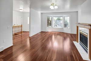 Unfurnished living room featuring a fireplace, a textured ceiling, dark wood-type flooring, and a chandelier