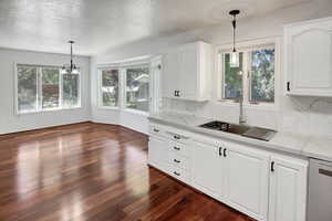 Kitchen featuring decorative backsplash, light stone countertops, white cabinetry, decorative light fixtures, and a textured ceiling