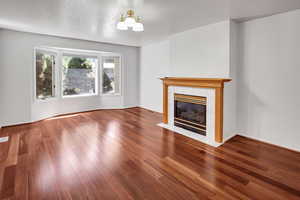 Unfurnished living room featuring a fireplace, dark wood-style flooring, a textured ceiling, and a chandelier