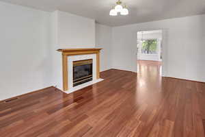 Unfurnished living room with dark wood-style floors, a chandelier, and a fireplace