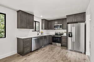 Kitchen with stainless steel appliances, dark brown cabinets, light wood finished floors, and a textured ceiling