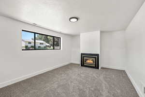 Unfurnished living room with carpet floors, a glass covered fireplace, and a textured ceiling