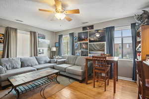 Living area featuring light wood finished floors, a textured ceiling, and ceiling fan