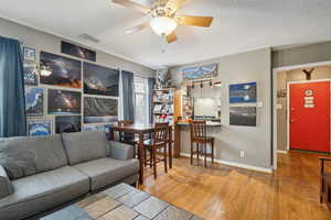Living room with a textured ceiling, light wood finished floors, and ceiling fan