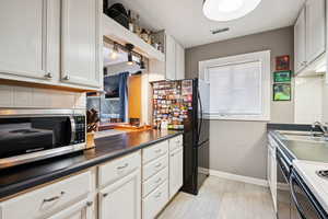 Kitchen featuring tasteful backsplash, dark countertops, black appliances, and white cabinets