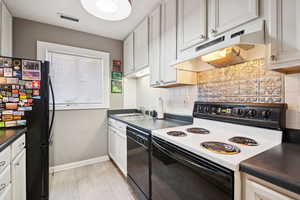 Kitchen with black appliances, dark countertops, tasteful backsplash, under cabinet range hood, and white cabinetry