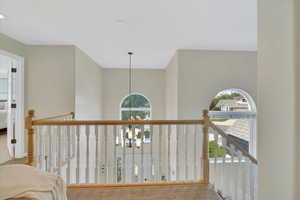 Hall featuring carpet, a chandelier, and an upstairs landing