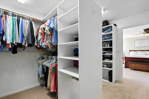 Spacious Main closet with light colored carpet and a ceiling fan