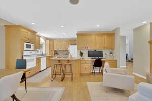 Kitchen featuring built in desk, light brown cabinetry, a kitchen breakfast bar, white appliances, and light wood-style floors