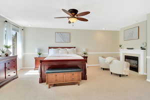 Bedroom with light colored carpet, a ceiling fan, and a glass covered fireplace