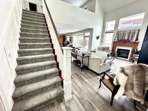 Living room with stairway, a glass covered fireplace, high vaulted ceiling, and light wood-type flooring