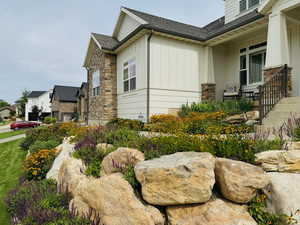 View of property exterior with board and batten siding, roof with shingles, stone siding, and covered porch