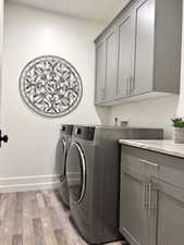 Washroom with light wood-type flooring, cabinet space, and washing machine and clothes dryer