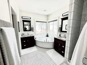 Bathroom featuring tile walls, two vanities, a bath, a stall shower, and light tile patterned flooring