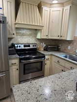 Kitchen featuring appliances with stainless steel finishes, light stone counters, and decorative backsplash