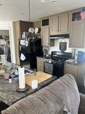 Kitchen with black appliances, glass insert cabinets, dark countertops, washer and dryer, and under cabinet range hood