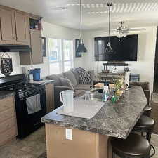 Kitchen with black gas range oven, a kitchen island with sink, a kitchen bar, pendant lighting, and under cabinet range hood