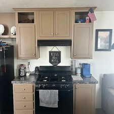 Kitchen featuring black appliances, dark countertops, glass insert cabinets, open shelves, and ventilation hood